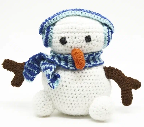 Bonhomme de neige en crochet blanc et vert avec chapeau et écharpe bleus, nez orange et bras marron